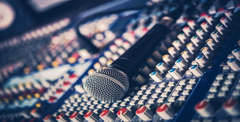 A close-up of a microphone resting on an audio mixing console, surrounded by colorful knobs and sliders used for church live stream audio mixing and control.